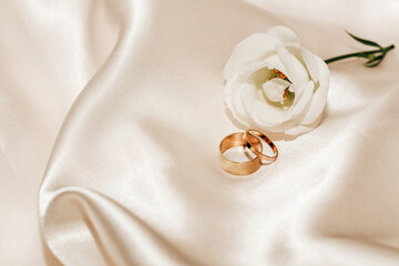 Wall Mural - White rose on a silk beige background with gold jewelry wedding rings, space for text.