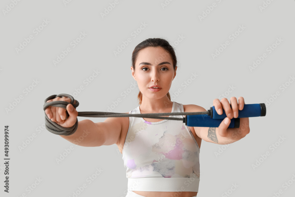 Sporty young woman with skipping rope on grey background