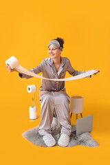 Wall Mural - Young woman in pajamas and with paper sitting on toilet bowl against color background