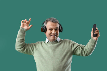 Canvas Print - Senior man in headphones with mobile phone dancing on green background