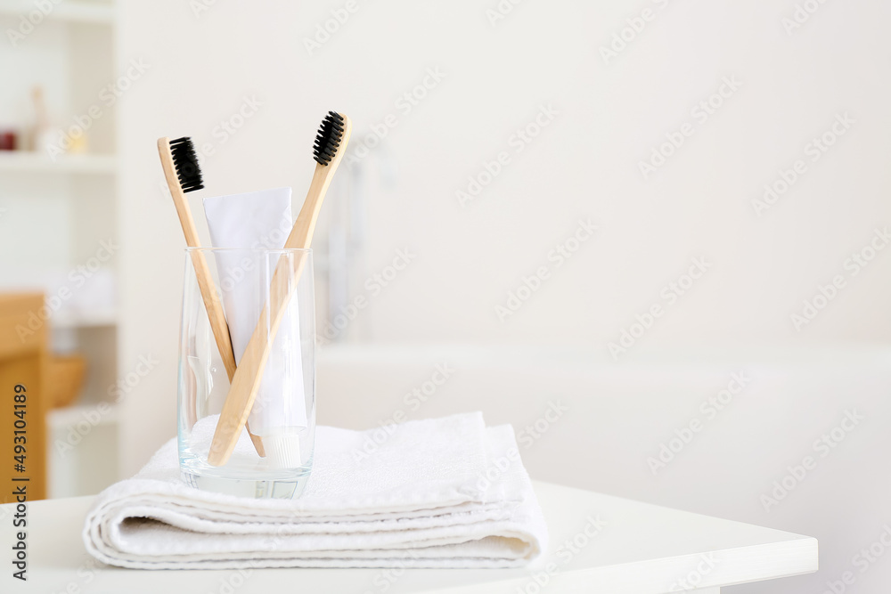 Holder with toothbrushes, towel and toothpaste on table in bathroom