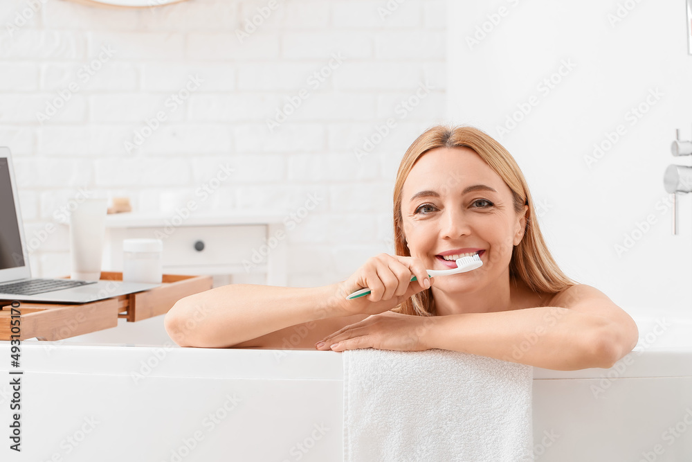 Beautiful mature woman brushing teeth while taking bath in morning