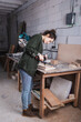 © LIGHTFIELD STUDIOS - Side view of young furniture designer working with electric drill and wooden plank in workshop.
