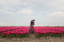 Woman In Floral Dress Standing In Field Of Colorful Pink Tulips In Spring