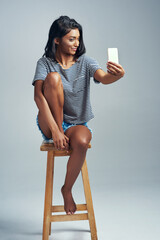 Sticker - Darling, youre different. Studio shot of a beautiful young woman taking a selfie while sitting on a wooden stool.