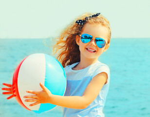 Wall Mural - Summer portrait of happy smiling little girl child playing with inflatable water ball on beach over sea