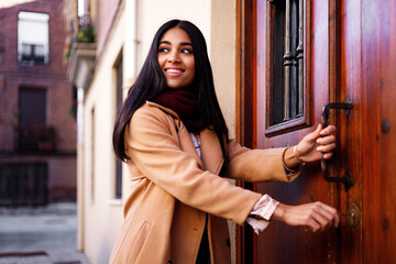 Wall Mural - young happy indian woman opening her home door and looking back with joy, copy space