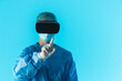 © PoppyPix - Professional doctor wearing virtual reality glasses focus on the foreground finger, isolated studio shot with blue background. High quality photo