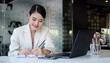 © wattana - Beautiful asian businesswoman using laptop computer and checking financial document at office desk.