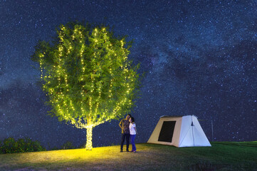 Wall Mural - couple under a tree adorn lights beside tent camping at night. there are milky way galaxy stars in t