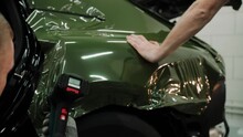 Two Men Are Vinyl Wrapping A Car In Dark Green Color. Process Of Vinyl Wrapping A Car In A Car Studio, Using Heat Gun To Stretch The Film. Dark Green Car Vinyl Wrap. High Quality 4k Footage