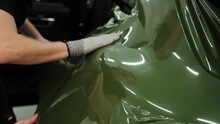 Slow Motion Shot Of Man Vinyl Wrapping The Car, Smoothing The Wrap With His Hands. Process Of Wrapping A Car In A Garage. Dark Green Vinyl Car Wrap. High Quality 4k Footage