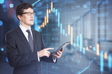 Sticker - Attractive worried young businessman using tablet while standing in blurry office interior with abstract falling candlestick forex chart. Trade, economy and crisis concept. Double exposure.