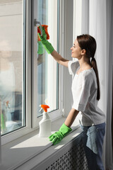 Young woman cleaning window glass with rag at home