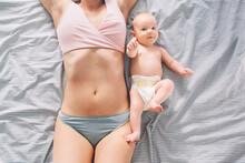 The Postpartum (or Postnatal) Period. Young Mother With Visible Postpartum Body Marks And Her Cute Little Baby. Two Months Baby Lying Near At Mother Belly On Bed. Skin To Skin.