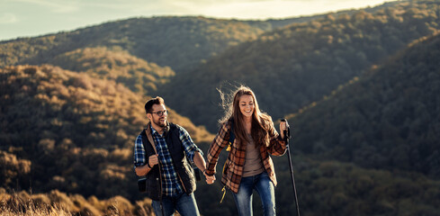 couple with backpacks hiking together in nature on autumn day.