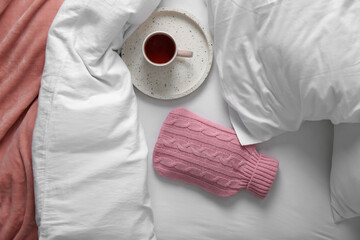 Poster - Hot water bottle with knitted cover and cup of tea on bed, flat lay