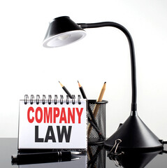 Poster - COMPANY LAW text on notebook with pen and table lamp on the black background