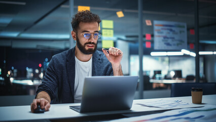 Successful Handsome Creative Director Working on Laptop Computer in Big City Office Late in the Evening. Businessman Preparing for a Marketing Plan in Conference Room.