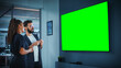 © Gorodenkoff - Company Operations Manager Holds Meeting Presentation for a Team of Executives. Adult Male Uses Wide TV Set with Horizontal Green Screen Mock Up Display. People Work in Business Office.