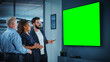 © Gorodenkoff - Company Operations Manager Holds Meeting Presentation for a Team of Executives. Adult Male Uses Wide TV Set with Horizontal Green Screen Mock Up Display. People Work in Business Office.