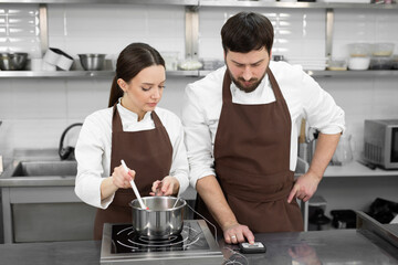 Man and woman confectioners prepare dessert together in a professional kitchen, cook syrup and cream.