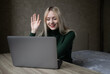 © Екатерина Бучинская - Emotional cheerful blonde girl in green golf is talking via video link at an online conference. Works at home with a laptop. Sits at the table in a positive mood in the room. Online learning. High