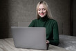 © Екатерина Бучинская - Happy smiling blonde girl in green golf joyfully works online at home with a laptop. Sits at the table in a good mood in the room. High quality photo