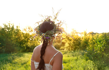 girl in flower wreaths on meadow, sunny green natural background. floral crown, symbol of summer sol