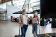 © malajscy - Two travelling women wearing protective masks discussing by flight information board at the airport