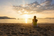 © jayzynism - Single young woman sitting alone and looking through the sea on the beach.