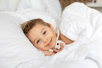 Sticker - Beautiful blond toddler child, boy, sleeping in bed with teddy bear toy