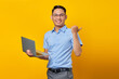 © Bangun Stock Photo - Portrait of handsome smiling Asian man in glasses using laptop and pointing fingers at copy space isolated on yellow background. businessman and entrepreneur concept
