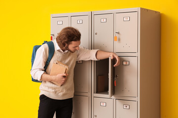 Canvas Print - Male student with books near locker on yellow background