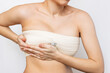 © Марина Демешко - Cropped shot of young woman with elastic bandage after breast augmentation with silicone implants isolated on white background.The result of lifting. Breast size correction. Pain after plastic surgery