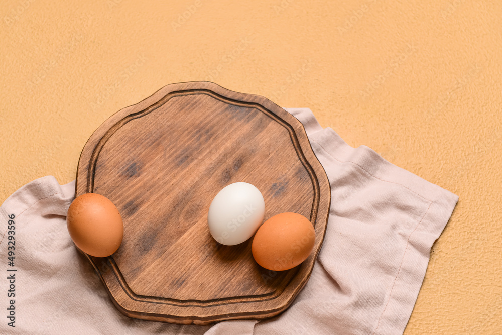 Wooden board with fresh chicken eggs on beige background