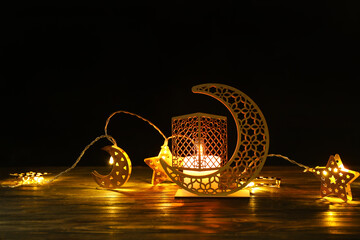 Arabic candle holder with glowing candle and garland on table against dark background