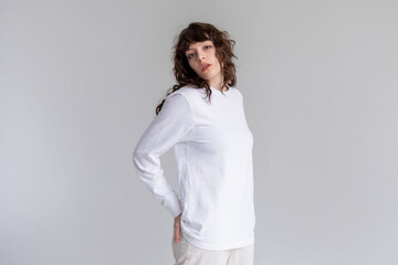 Young woman with curly hair in a white long sleeve t-shirt stands on a white background. Mock-up.