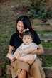 © Erin Brant/Stocksy - Asian baby sitting on mother's lap  outdoors