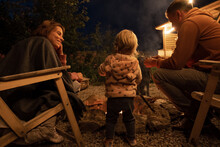 Toddler With Parents Resting Near Fire Pit At Night