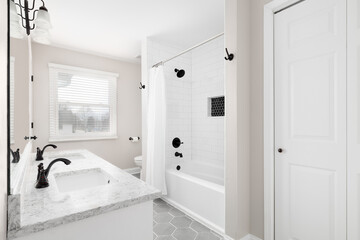 A renovated bathroom with a white vanity, grey hexagon tiled floor, marble countertop, and a shower with white subway tiles.