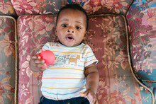Adorable Black Baby With Toy On Settee
