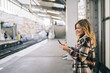 © Daniel Gonzalez/Stocksy - Smiling lady texting on railway platform