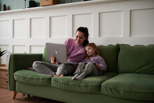 Mom Working On Laptop On Couch, With Daughter