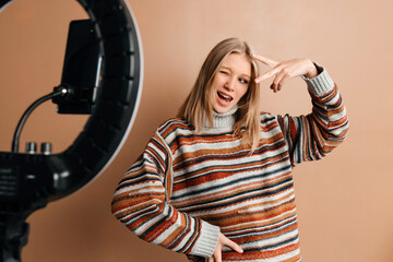 The girl is having fun while making photos for her blog. Young woman is using a mobile phone and a ring light to take photos. Concept of blogging