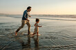 © Erin Brant/Stocksy - Father chasing daughter in ocean at sunset
