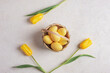 Basket with yellow painted eggs and tulips on white textured background. Easter concept. Top view, flat lay