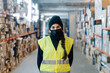 © Sergio Marcos/Stocksy - Woman wearing mask standing between racks in warehouse