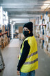 © Sergio Marcos/Stocksy - Woman wearing mask standing between racks in warehouse