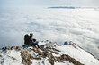 © Alina Miluseva/Stocksy - Adult male hiker sitting on rocky mountain above clouds
